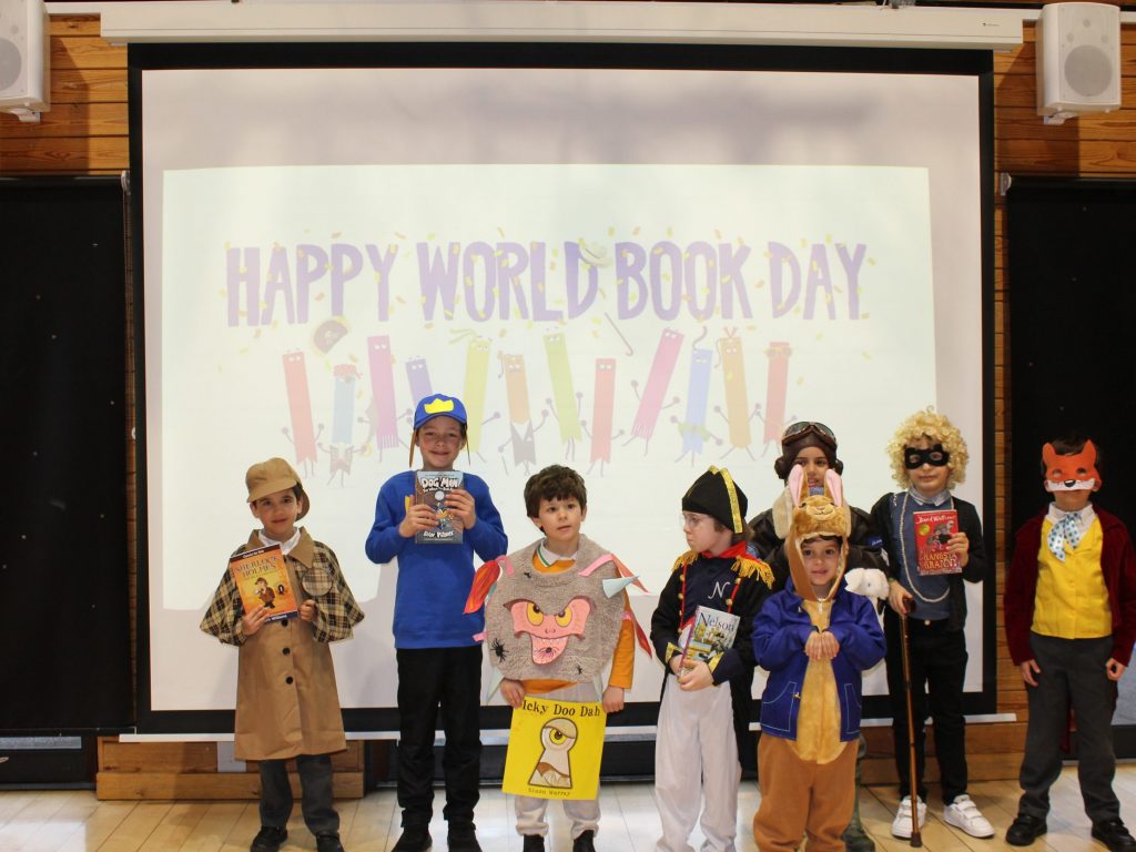 Seven school children wearing different costumes, stood in front of a projector screen.