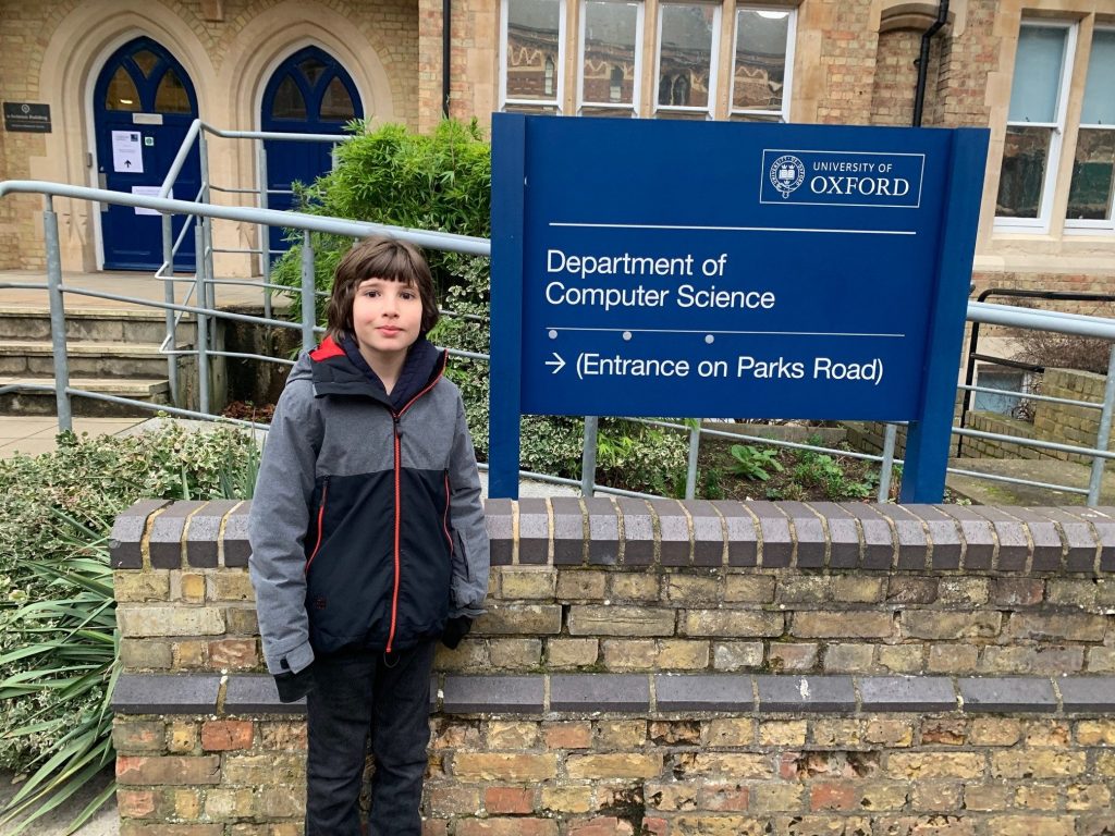 A child stood outside a sign for the Department of Computer Science at The University of Oxford.